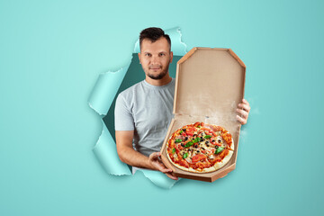 A man holding a pizza in his hands punching a blue paper background. Fast delivery concept, ready food, modern world.