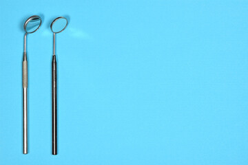 Two medical dental mirrors on blue background with copy space. Flat lay close up top view on dental equipment.