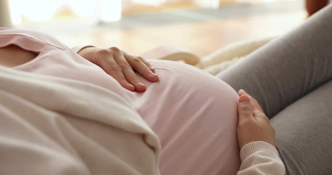 Close up calm young pregnant woman holding hands on belly, relaxing breathing fresh air at home, enjoying carefree moment alone at home, showing love and care to unborn baby, motherhood concept.