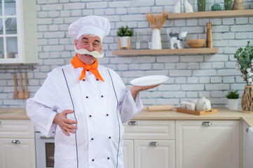 An old man with a bushy gray mustache in a chef's hat is cooking in the kitchen.