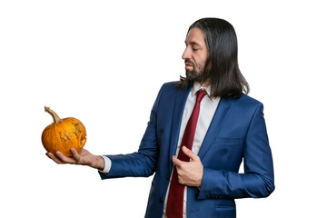 A man with a beard and long hair in a jacket and shirt with a  Halloween pumpkin in his hands posing on a white background. Various poses and emotions. Halloween concept. 