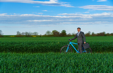 Businessman rides a bicycle in a green grass field - business concept for freedom, vacation or freelance. Beautiful spring nature.