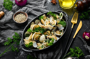Boiled shellfish in shells with garlic and parsley in a black plate. Seafood. Top view. Free space for text.
