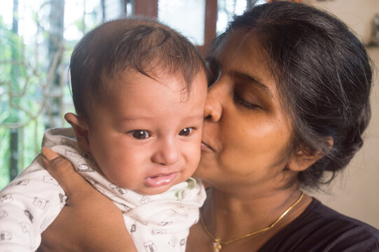 Happy Baby Loves mom Kisses. Loving Mother kissing cute little adorable kid on her lap. Close-up portrait. Indian ethnicity. Front view. Happy parents day Motherhood parenthood togetherness background