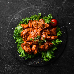 Veal stewed with vegetables in wine on a black stone plate. Top view. On a black background.
