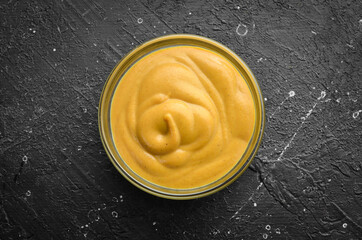 Mustard sauce in a bowl on a black stone background. Top view. Free copy space.