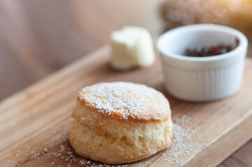 Butter scone top with icing sugar serve with straberry jam and fresh cheese on wooden plate, homemade bakery scone prepare for tea break, tea time.