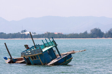 Local fishing boat capsized at the sea, shipwreck in ocean, wooden boat accident.