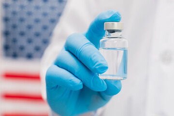 Doctor holding vaccine bottle with USA flag background.