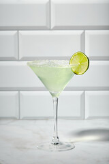 Martini cocktail with ice and slice of lime on marble table background. Alcoholic cocktail or non-alcoholic mocktail.