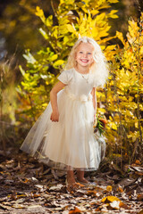 Obraz na płótnie Canvas A little girl in white dress who smiles on a background of yellow leaves