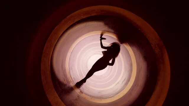 A silhouette of beautiful sexy girl , woman dancing inside circle tube . Against colored & gray background . Real decoration . None computer graphics . Shot on Arri Alexa Cinema Camera in 4K .