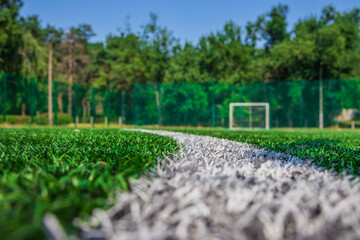 Soccer field with artificial green grass near the school. Amateur football field. Sunny summer day. Soft focus