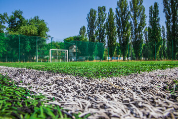 Soccer field with artificial green grass near the school. Amateur football field. Sunny summer day. Soft focus