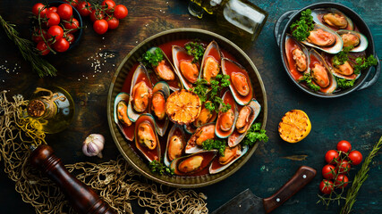 Metal tray with mussels cooked in tomato sauce with garlic, parsley and lemon. On a black stone background.