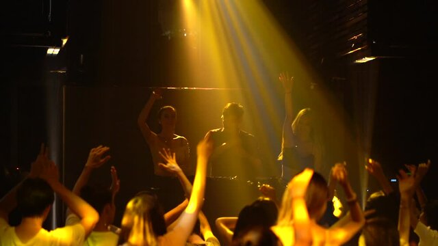 Young Asian DJ male performing in nightclub with dancing people.
