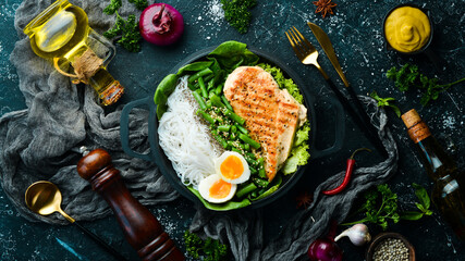 Baked chicken fillet with rice pasta, spinach and beans in a black stone plate. Dietary food. Top view. Free space for text.