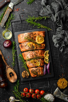 Salmon. Pieces of grilled fish on a black stone background. Recipe. Seafood. Free space for text.