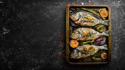 Baked dorado fish with asparagus and vegetables in a metal tray. Free copy space. On a black stone background.