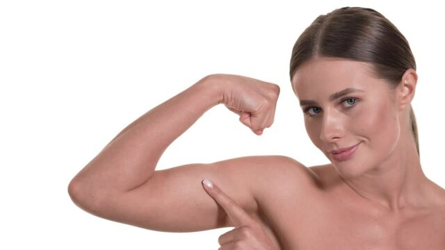 Portrait of a caucasian woman, flexing her biceps, tapping it and smiling. Health concept, white background.