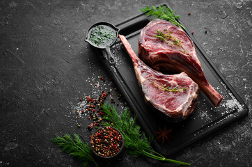 Two raw steaks on the bone with spices. On a black stone background. Top view. Free copy space.