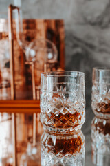 Two glasses of whiskey stand on a mirrored bar counter.