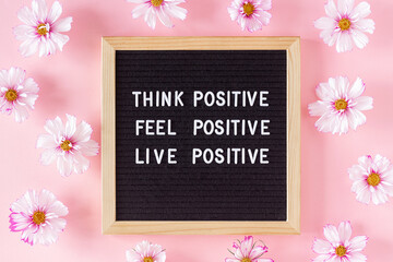 Think positive, feel positive, live positive. Motivational quote on letter board and flowers on...