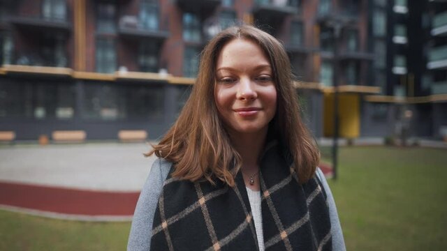 Portrait of a gorgeous dark haired woman smiling charmingly while standing against the background of modern buildings. Happy young woman enjoys life. Slow motion