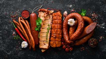 Set of sausage, salami and smoked meat with rosemary and spices on a black stone background. Top view. Free space for text. - obrazy, fototapety, plakaty