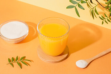 Orange juice glass and collagen powder on table with plant and shadow, top view