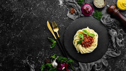 Spaghetti pasta with bolognese sauce and basil in a black stone plate. Italian food. Top view. Free space for text.