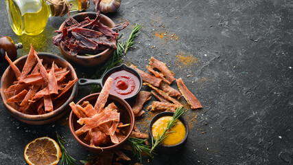 Jerky. Dried meat slices with spices and herbs. Snacks for beer On a black stone background. Top...