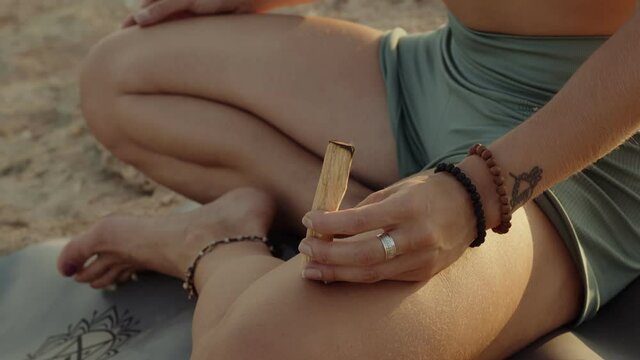 European anonymous girl sit in yogi pose on a rocky ground with sacred wood stick burn in her hand. Warm calm, relax atmosphere of a ritual. High quality extreme closeup video footage.