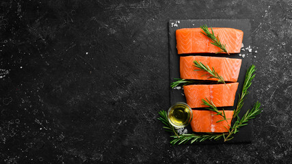 Raw salmon with rosemary, lemon and vegetables on a black stone background. Seafood. Top view. Free...