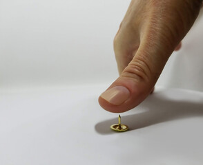 Photo of a thumb getting ready to push down on a thumb tack with white background and shadow