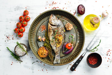 Fototapeta na wymiar Delicious baked whole fish with herbs and lemon in a metal baking tray. Dorado. On a white wooden background.