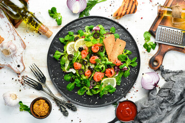 Fresh salad with salmon and olives in black plate. Top view. Free space for your text. Rustic style.