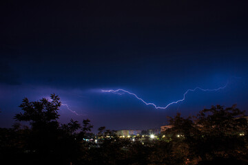 Lightning discharges during a large rainstorm in a city with forest fringes