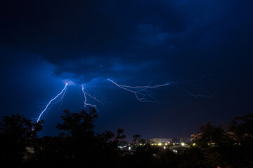 Fototapeta na wymiar Lightning discharges during a large rainstorm in a city with forest fringes