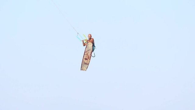 Young adult caucasian fit male person enjoy riding kite surf board macking extreme trick stunt bright sunny day against blue sky at sea or ocean shore. Watersport adrenaline fun adventure acitivity