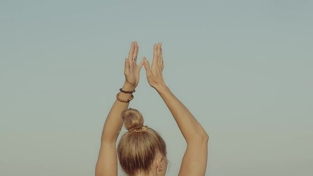 Back view of young woman doing prayer pose while practicing yoga overlooking mediterranean sea at sunset. Meditation for mental and physical health. Calm meditative ambient. Slow motion video footage.