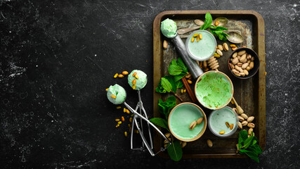Pistachio ice cream with mint and pistachios. Ice cream spoon. On a black stone background, top view.