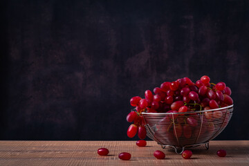 bunch of grapes in bowl or basket on wooden table with black background dark mood and tone.