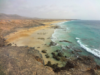 Scenic view of the beautiful yellow sand beach with some black volcanic rocks on Fuerteventura island, Canary Islands, Spain.