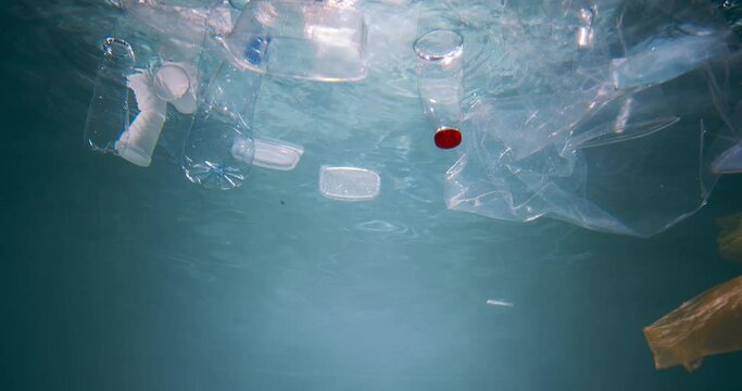 Plastic packaging waste. Cinematic view of various garbage floating under water in beautiful sun light rays slow motion.
