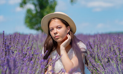 Street portrait of a serious young girl 17-20 years old in a white dress and straw hat with long black hair against the sky and lavender field, looking at the camera.