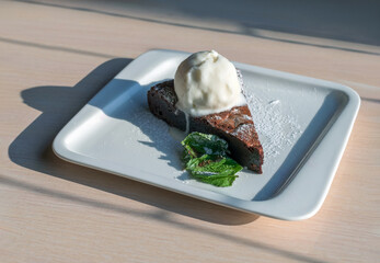 Chocolate brownie with an ice cream on a white plate on a wooden table.