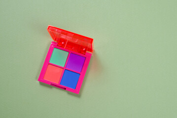 Purple, green, orange and blue eye shadow palette on a green background. Make up. Neon colours.