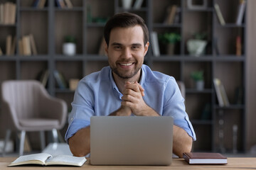 Business person. Motivated young man entrepreneur sit at home office workplace look at camera smile enjoy doing freelance job. Portrait of happy enthusiastic guy student successful in distant learning