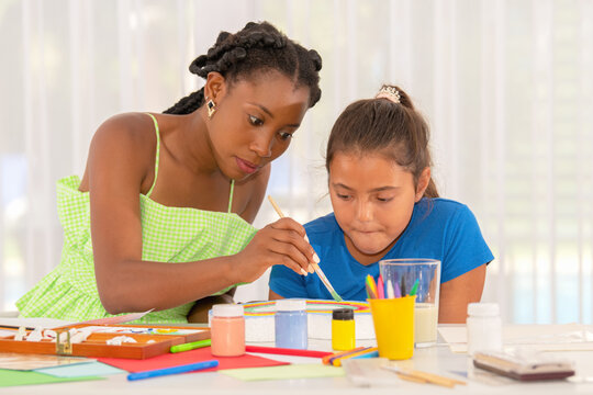 African American teacher helping to paint to latin student girl in art class